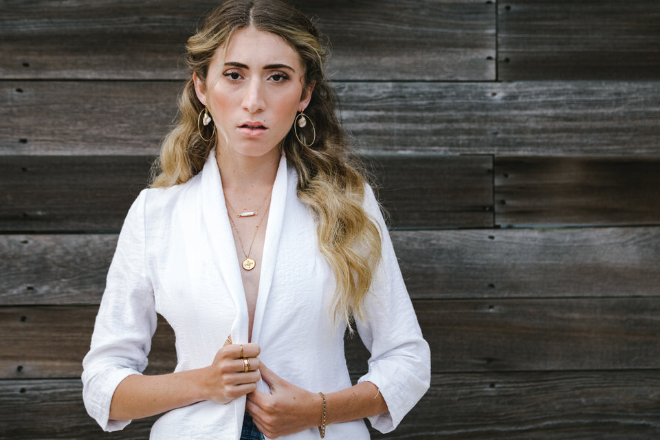 Whim Jewelry summer collection featuring model with gold hoop earrings, layered gold necklaces, and stackable gold rings. Model and jewelry are modern, bohemian, and delicate. Everything is made by hand by Whim Founder Jaime Huizing.